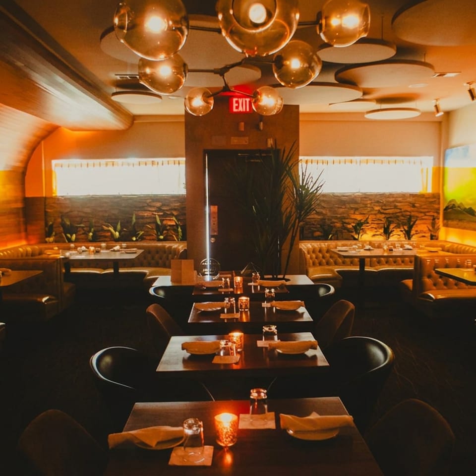 Warmly lit restaurant dining room with set tables, leather booths, desert murals, and sculptural globe pendant lights.