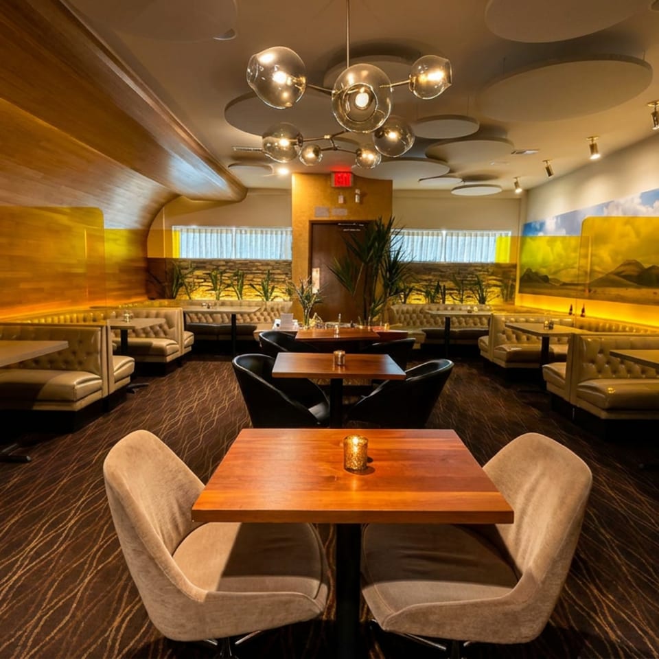 Upscale restaurant dining room with tufted leather booths, wooden tables, warm lighting, and landscape wall murals.