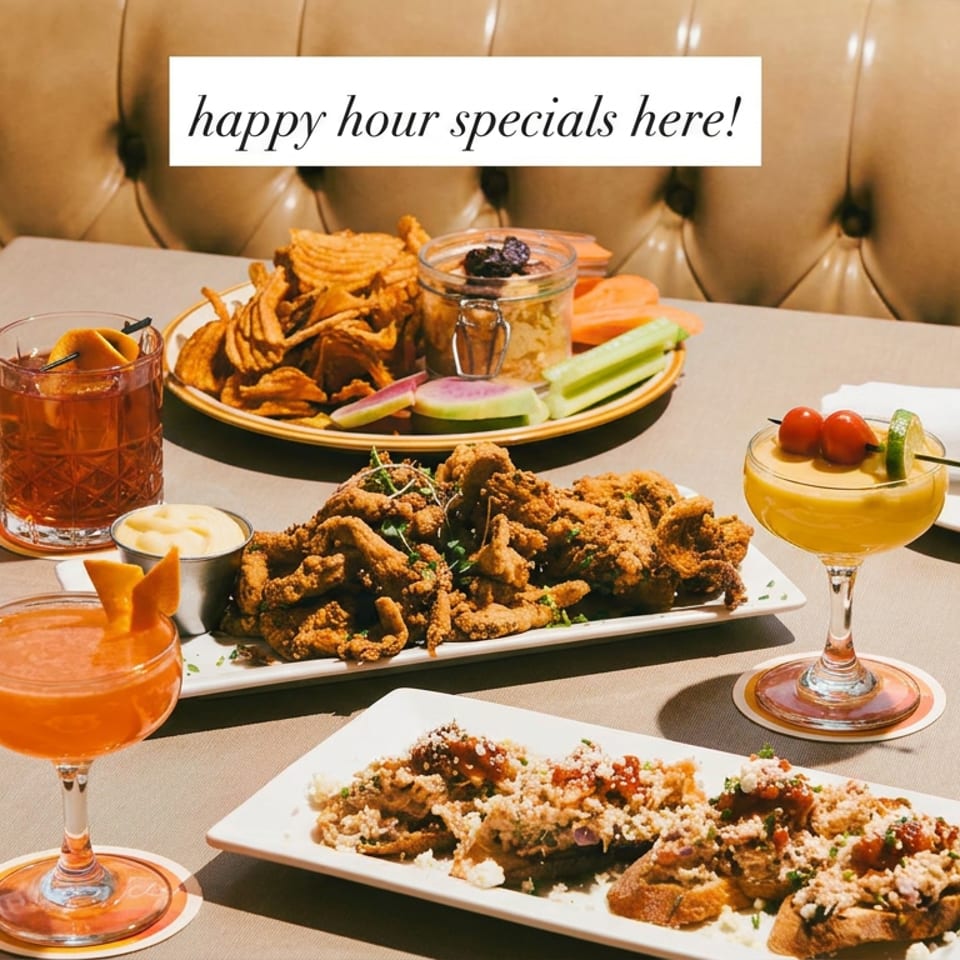 Happy hour spread of fried dishes, dipping sauces, and colorful cocktails on a restaurant table beside a tufted leather booth.