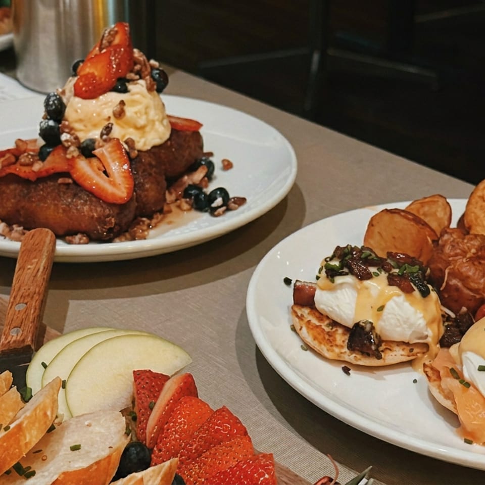 Brunch spread featuring eggs Benedict, roasted potatoes, salad, berry-topped French toast, fruit, cheese, and toasted bread.